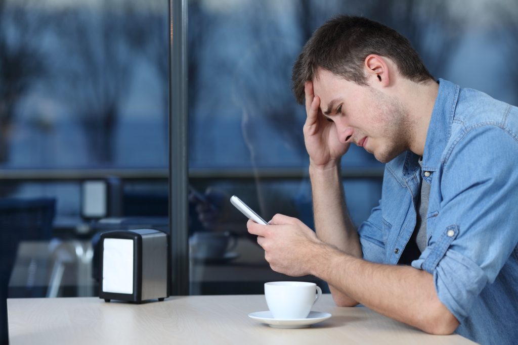 Sad man checking phone message in a coffee shop